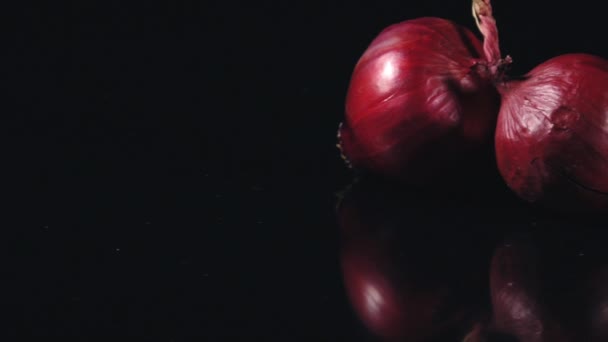 黒い鏡のテーブルに新鮮な赤玉ねぎ 黒い背景に赤玉ねぎ スローモーションクローズアップフードビデオ — ストック動画