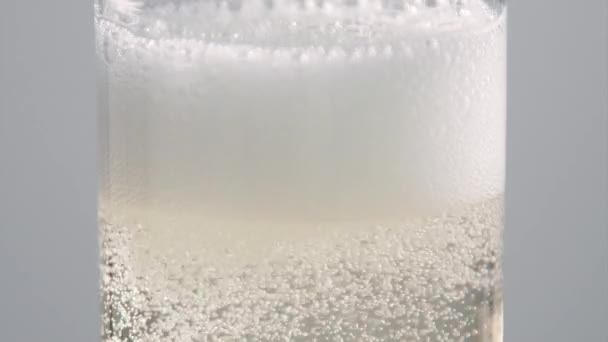 Du macro champagne. Le champagne coule dans le verre. Quelqu'un verse du vin mousseux dans le verre. Tournage serré du champagne coulant sur fond blanc . 