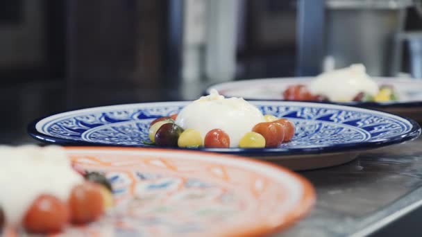 在一块明亮的盘子里放一个面包奶酪 放在西红柿上 意大利餐厅的一道菜 餐厅菜单 伯拉塔奶酪与樱桃番茄 桌子上的成品菜 — 图库视频影像