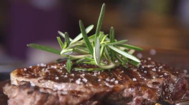 Meat steak. Meat and rosemary. A close up of a steak with sea salt and herbs. Steak on a wooden board in a restaurant.  Serving a steak at a meat restaurant.