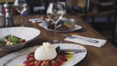 Domates ve fesleğenli burrata. Restoranın masasında güzel bir tabak ve bir bardak şarap duruyor. Restoranda servis edilen Burrata tabağı. Bir tabak şarapla güzel bir kompozisyon..