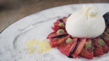 Domates ve fesleğenli burrata. Restoranın masasında güzel bir tabak ve bir bardak şarap duruyor. Restoranda servis edilen Burrata tabağı. Bir tabak şarapla güzel bir kompozisyon..