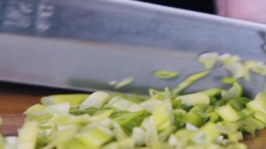 Şef yeşil soğan makro atışı yapıyor. Yeşil soğan ve bıçak yakın çekim. Eller soğanı yavaş çekimde kesiyor.. 