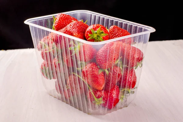 Transparente Plastikdose mit roten reifen saftigen Erdbeeren auf einem Tisch — Stockfoto