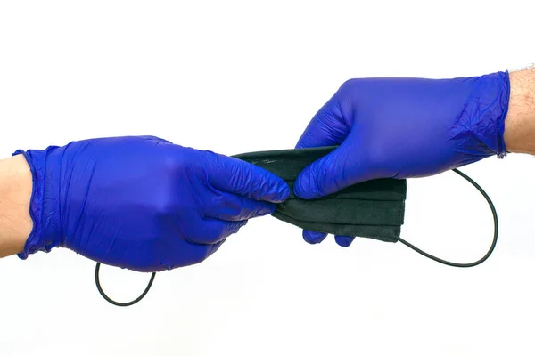 Hand in blauem medizinischen Schutzhandschuh überträgt eine schwarze medizinische Maske auf eine andere behandschuhte Hand auf weißem Hintergrund — Stockfoto