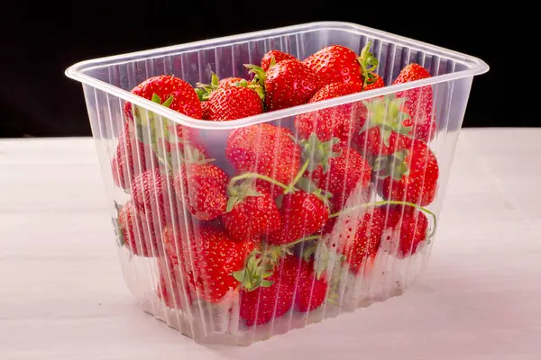 Transparente Plastikdose mit roten reifen saftigen Erdbeeren auf einem Tisch — Stockfoto