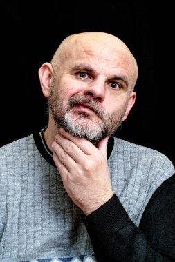 Siyah arka planda gri sakallı bir adam sakalını sıkar ve yüzünü buruşturur.