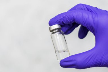 Mavi koruyucu ameliyat eldivenli bir doktorun elinde aşı olan şişe.