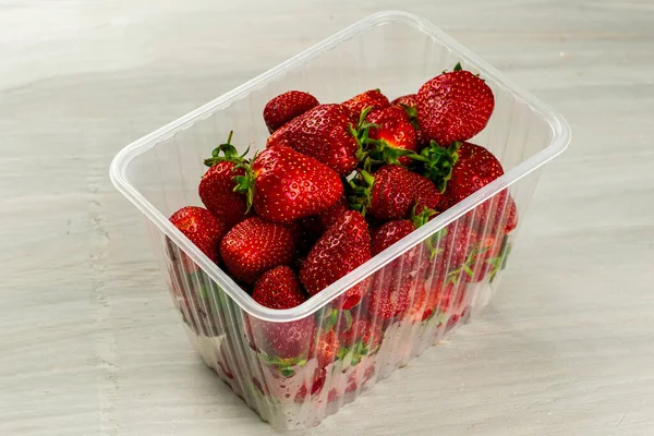 Ein klares Plastikgefäß mit reifen saftigen roten Erdbeeren steht auf dem Tisch — Stockfoto