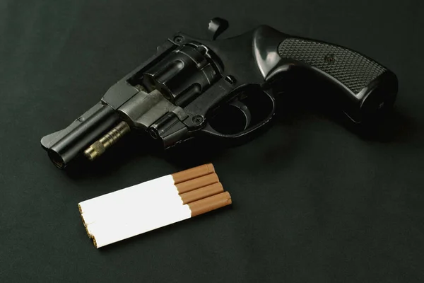 Concept smoking - suicide pistol lying on the dark background next to cigarettes tkmny key — Stock Photo, Image