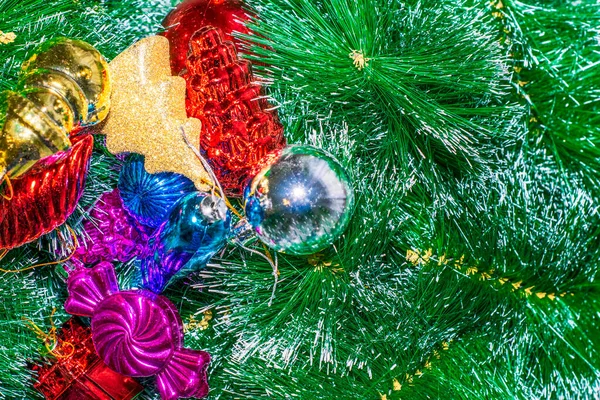 Multicolored Christmas toys lie on the artificial green spruce branches — Stock Photo, Image