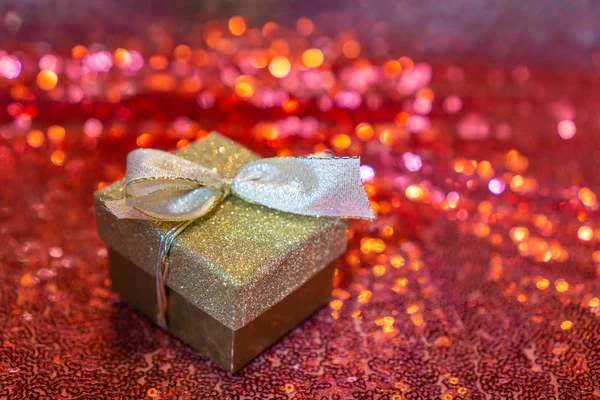 Golden box with ribbon on red glittering background