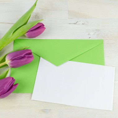 Yeşil bir zarf kağıt, mor laleler yanında beyaz bir levha ile