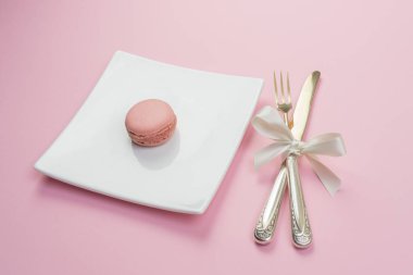 Bir pembe macaron, gümüş ve pembe bir arka plan beyaz bir tabak