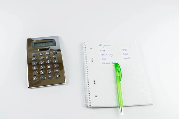 pocket calculator, next to it a writing pad with pencil, on it the German words for expenses, rent, insurance, car and foodstuffs