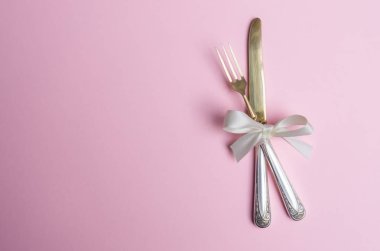 Çatal ve bıçak pembe bir arka plan üzerinde beyaz saten kurdele ile