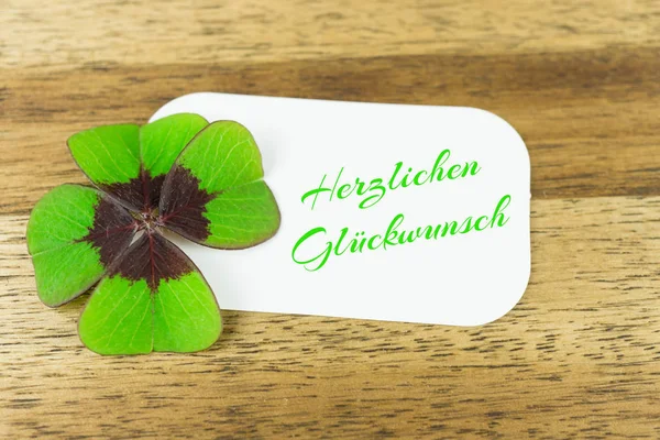 Four leaved clover with white label and the German words for congratulations