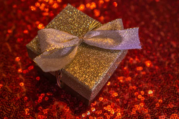 Golden gift box with ribbon and red glittering background