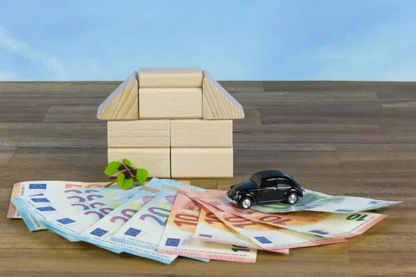 Banknotes, toy car and a house from wooden blocks as symbols for wealth