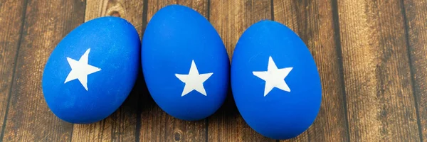 Blue easter eggs with white stars on wood background, banner