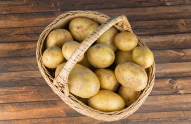 Tahta bir masanın üzerinde taze patateslerle dolu sepet, yukarıdan görüş.