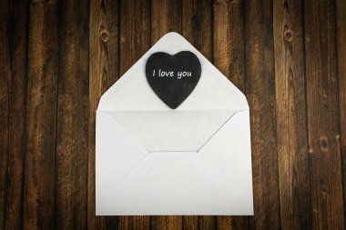 Siyah kalpli beyaz bir zarf ve seni sevdiğim kelimeler, arka plan olarak tahta masa.