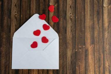 Kırmızı kalpli beyaz bir zarf, arka plan olarak ahşap masa