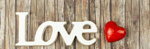 The word love in wooden letters with a white heart beside, banner and wooden background