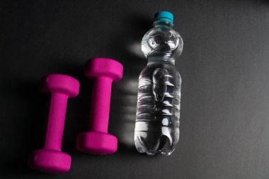 İki pembe dambıl ve bir şişe su, siyah arka plan.