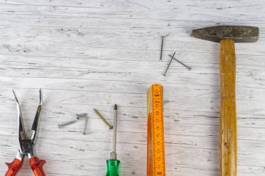 Beyaz ahşap arka planda el aletleri, çivili çekiç ve katlama kuralı, yanında farklı vida ve pense olan bir tornavida.