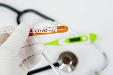 Üzerinde kan örneği olan bir laboratuvar tüpü ve Covid-19 izi olan bir el.