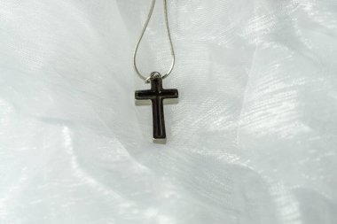Hassas beyaz organza kumaşının üzerinde siyah körfezi olan gümüş bir haç.