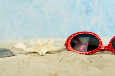 Kumda beyaz noktalı, kabuklu ve deniz yıldızlı kırmızı bir güneş gözlüğü.