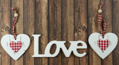 Tahta harflerle yazılmış aşk sözcüğünün yanında beyaz bir kalp, ahşap arka plan.