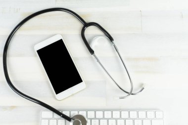 Steteskoplu bir cep telefonu ve ahşap bir masada bir bilgisayar klavyesi.