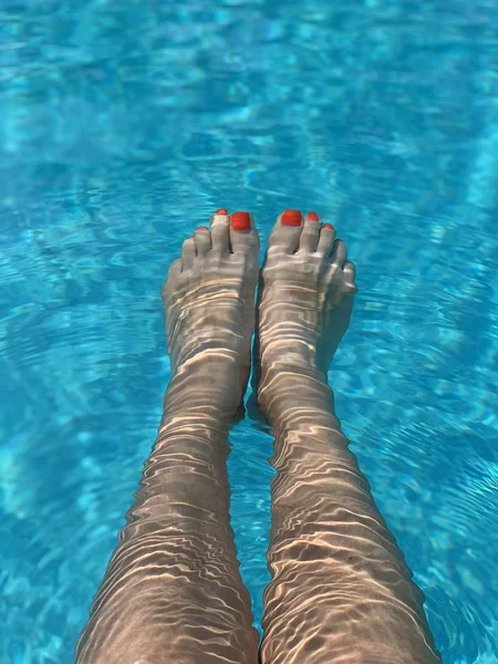 Pieds dans la piscine. Détendez-vous, vacances, été. Ongles rouges, peau bronzée, eau turquoise. La lumière du soleil danse dans l'eau. Vacances d'été, détente, plaisir, bronzage. Flottant à la surface — Photo