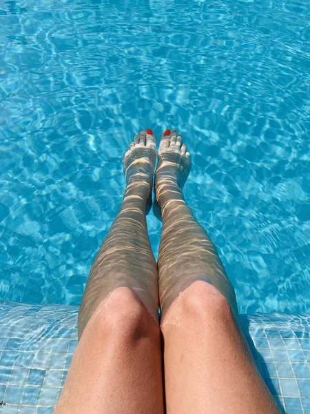 Piedi in piscina. Tranquillo, vacanza, estate. Unghie rosse, pelle abbronzata, acqua turchese. La luce del sole che danza nell'acqua. Vacanze estive, relax, divertimento, abbronzatura. Fluttuante sulla superficie — Foto Stock