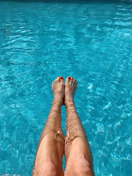 Feet in the swimming pool. Relax, vacation, summer. Red nails, suntanned skin, turquoise water. Sunlight dancing in the water. Summer holidays, relaxation, enjoyment, tanning. Floating on the surface