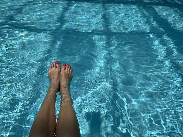 Pieds dans la piscine. Détendez-vous, vacances, été. Ongles rouges, peau bronzée, eau turquoise. La lumière du soleil danse dans l'eau. Vacances d'été, détente, plaisir, bronzage. Flottant à la surface — Photo