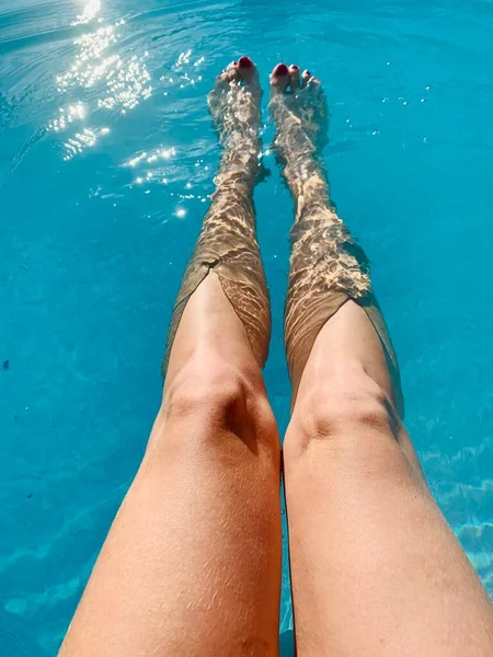 Woman\'s feet in a swimming pool with blue water