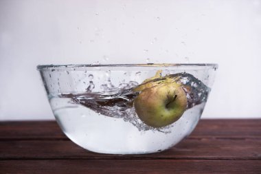 Yemek vurmak için alışılmadık bir açı. Islak taze elma. Elma bir kase suya düşer ve spreyler farklı yönlere uçar..