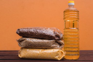 Bir şişe ayçiçeği yağı ve sarı arka plandaki bir pakette çeşitli tahıl gevrekleri ve mutfaktaki ahşap kahverengi bir tezgahın üzerinde