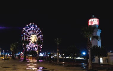 Georgia, Batumi. Geceleri kırmızı ışığı olan beyaz bir deniz feneri. Gece şehri, gece şehir ışıkları. Aydınlatılmış dönme dolap.