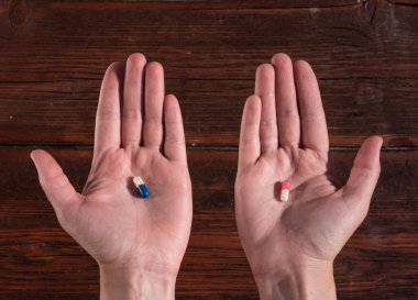 Bir insanın elinde iki tablet. Kırmızı ve mavi haplardan birini seç. İnsan sağlığı için vitaminler.