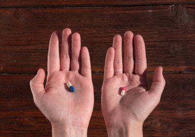 Bir insanın elinde iki tablet. Kırmızı ve mavi haplardan birini seç. İnsan sağlığı için vitaminler.