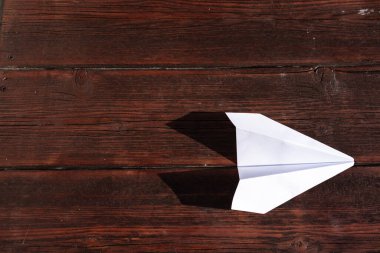 Tahta bir masanın üzerinde bir kağıt uçak yatıyor. Masada beyaz kağıt uçak, origami.