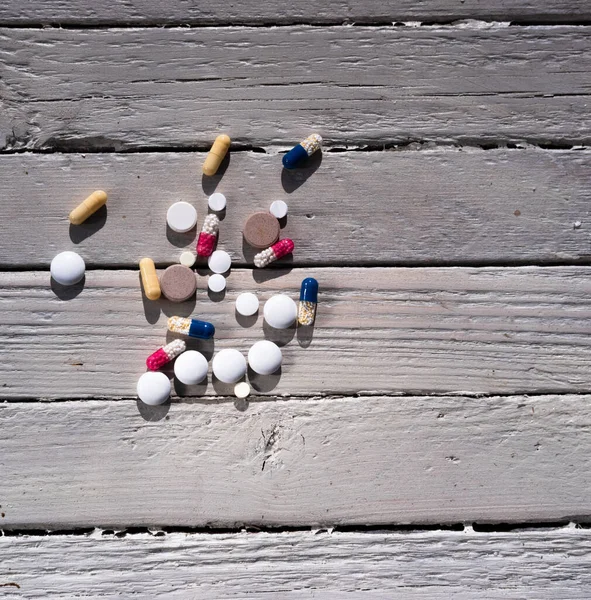 Many different tablets and vitamins on a wooden background. An old textured wooden table and pills.