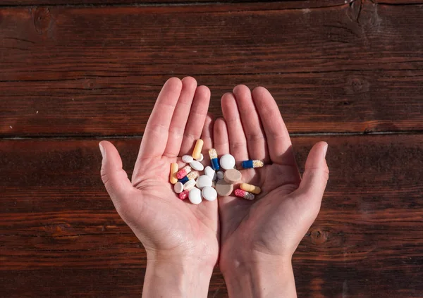 Many different tablets and vitamins in hands on a wooden background. An old textured wooden table and pills.