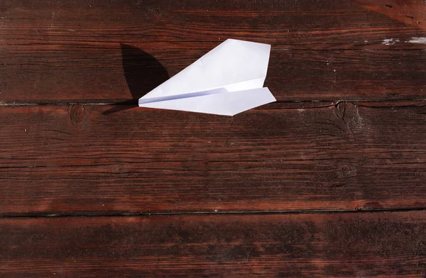 A paper airplane is lying on a wooden table. White paper airplane on the table, origami.