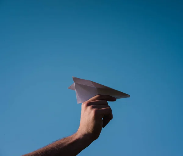Holding a paper airplane in your hand against the blue sky. The art of origami. White paper airplane.